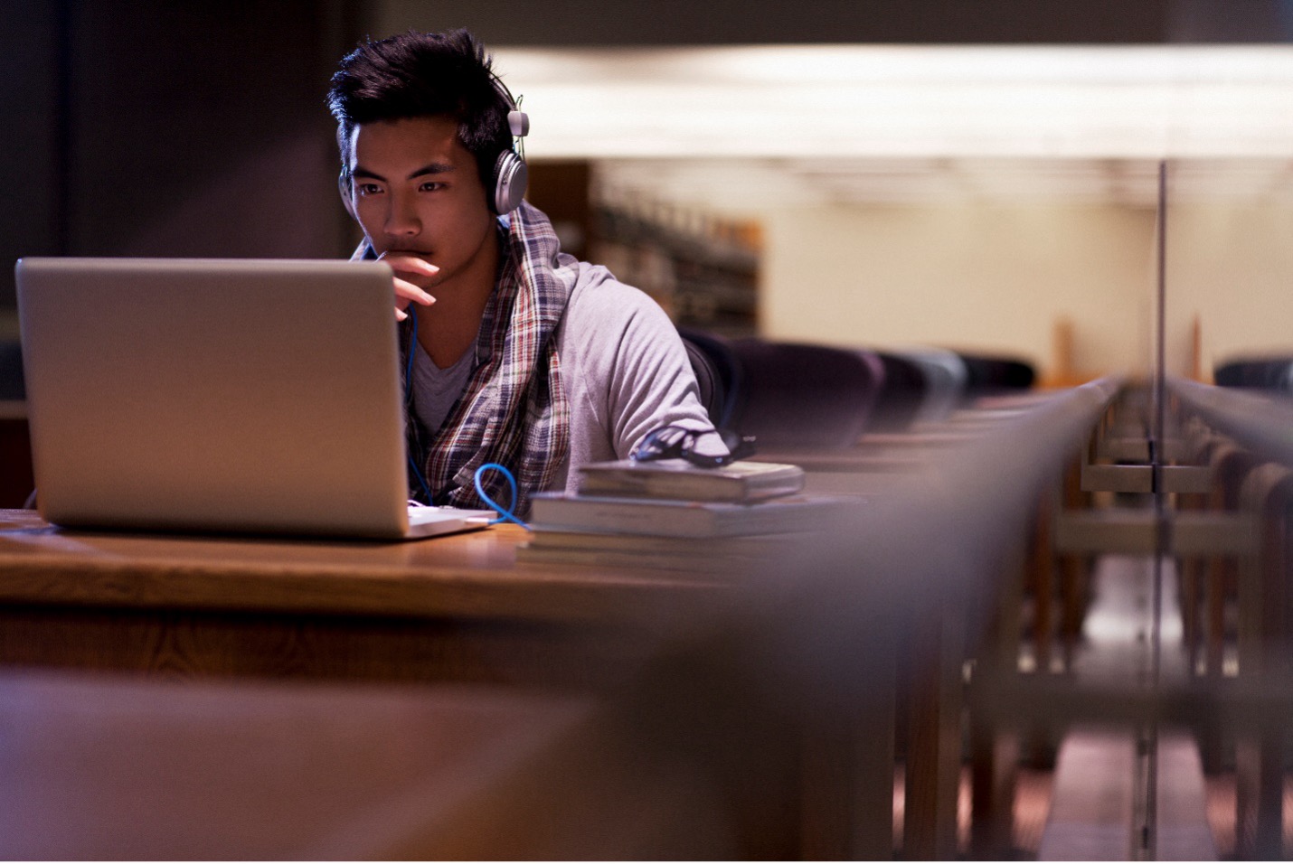 Male student with headphones on working on his laptop in the library